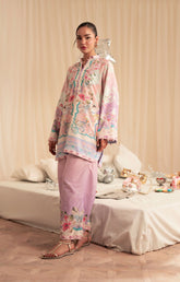 Woman in a floral outfit standing in a room with a bed and decorative items.